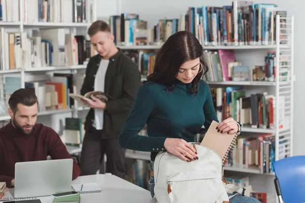 Studente donna imballaggio taccuino in borsa in biblioteca — Foto stock