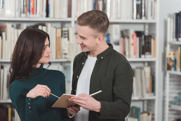 Улыбающаяся пара держит книгу в библиотеке и смотрит друг на друга — стоковое фото