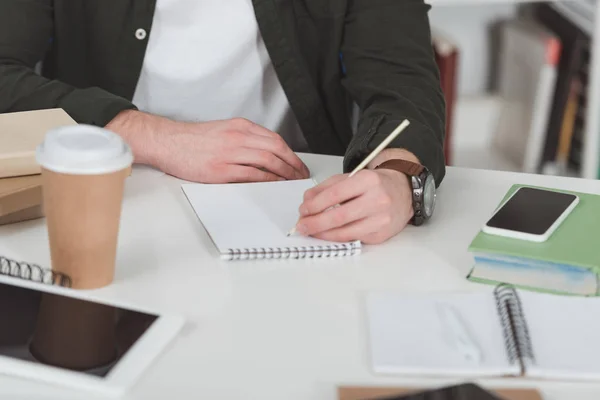 Cropped image of student making notes in library — Stock Photo