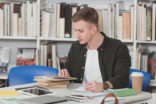 Student reading book and making notes in library — Stock Photo