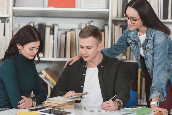 Amigos multiétnicos estudando na biblioteca e olhando para o livro — Fotografia de Stock