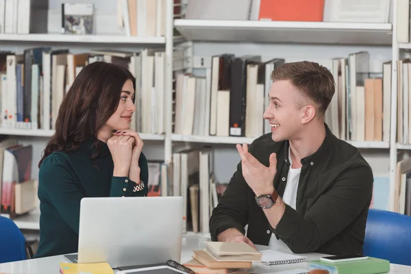 Studenti sorridenti che parlano a tavola in biblioteca — Foto stock