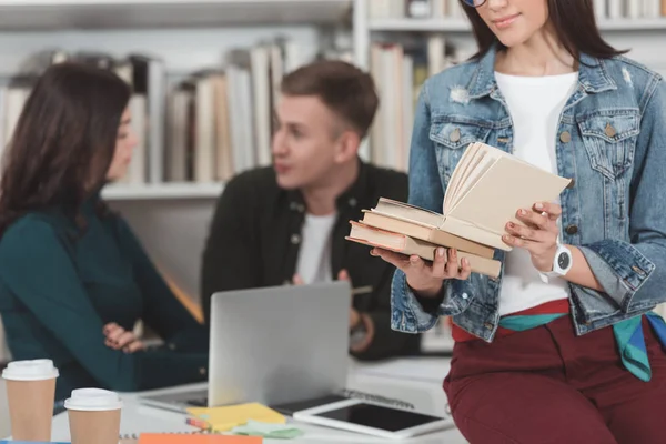 Imagen recortada de niña leyendo libro y sentado en la mesa en la biblioteca - foto de stock