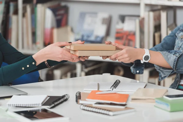 Cropped image of girl giving books to student in library — Stock Photo