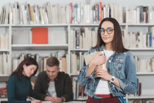 Chica afroamericana de pie con libros en la biblioteca - foto de stock