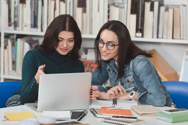 Multicultural amigos do sexo feminino olhando para laptop na biblioteca — Fotografia de Stock