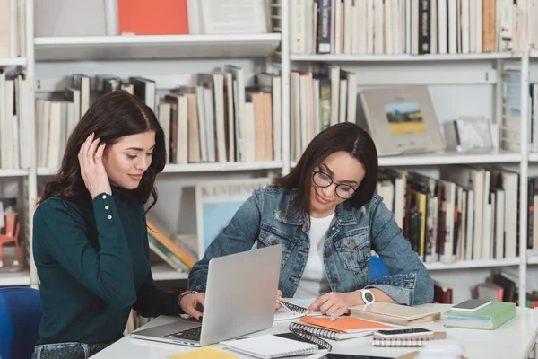 Amiche multiculturali che si preparano all'esame in biblioteca con laptop e libri — Foto stock