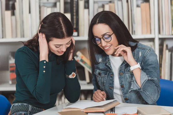 Amigos multiculturales leyendo libro en la biblioteca - foto de stock