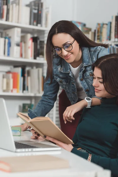 Amigos multiculturales leyendo libro en la biblioteca - foto de stock