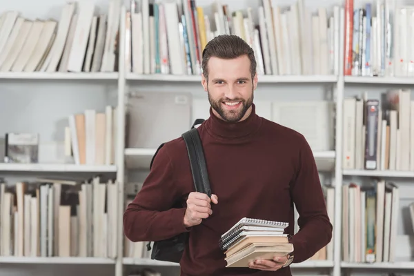 Guapo estudiante masculino con libros mirando la cámara en la biblioteca - foto de stock