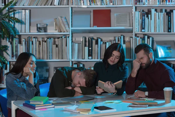 Втомлені багатоетнічні друзі, які навчаються в бібліотеці ввечері — стокове фото