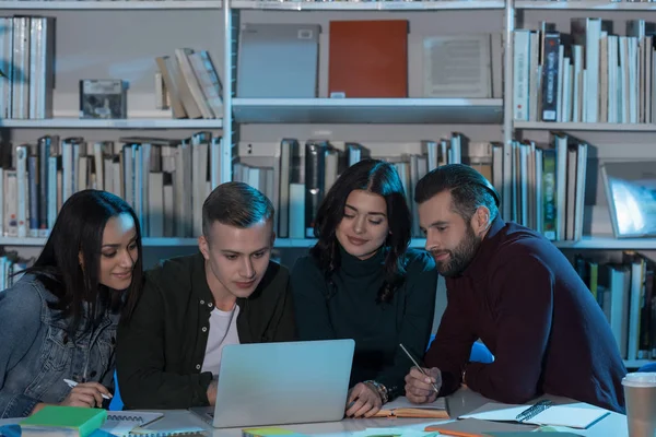 Amigos multiétnicos estudando com laptop na biblioteca — Fotografia de Stock