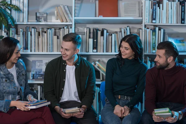 Four happy multicultural friends with books in library — Stock Photo