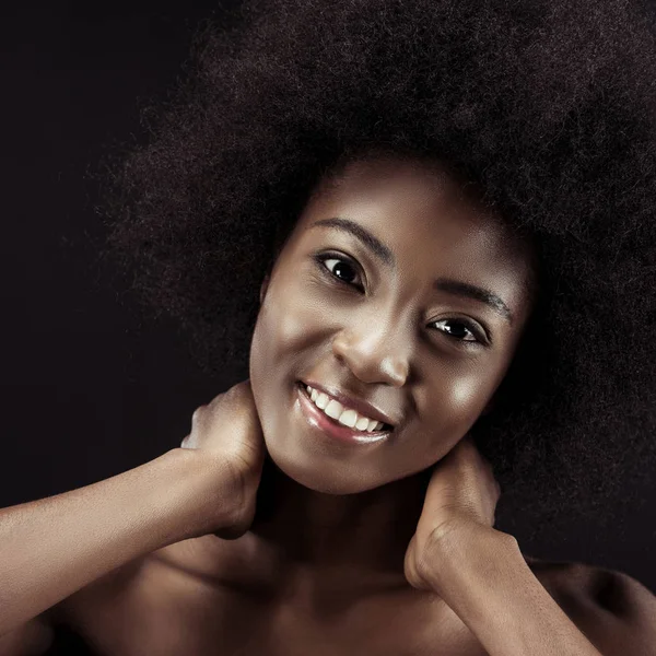 Mujer afroamericana feliz sosteniendo su cuello y mirando a la cámara aislada en negro - foto de stock