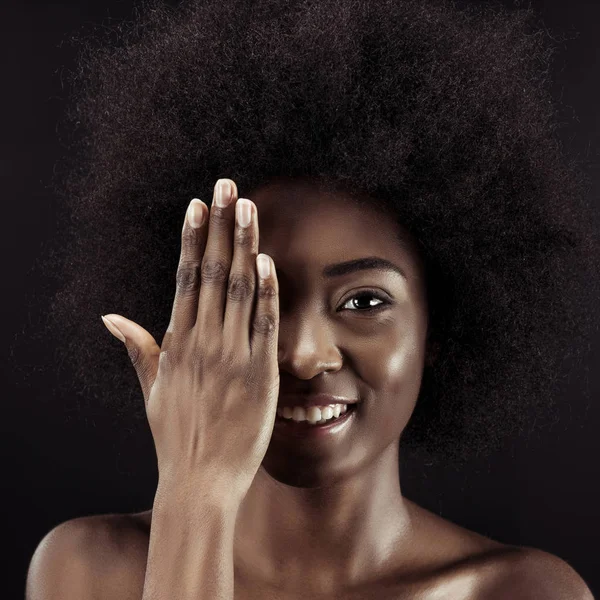 Glücklich afrikanisch-amerikanische Frau bedeckt Auge mit Hand isoliert auf schwarz — Stockfoto