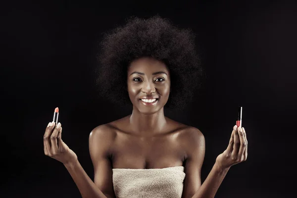 Hermosa mujer afroamericana sosteniendo lápices labiales aislados en negro - foto de stock