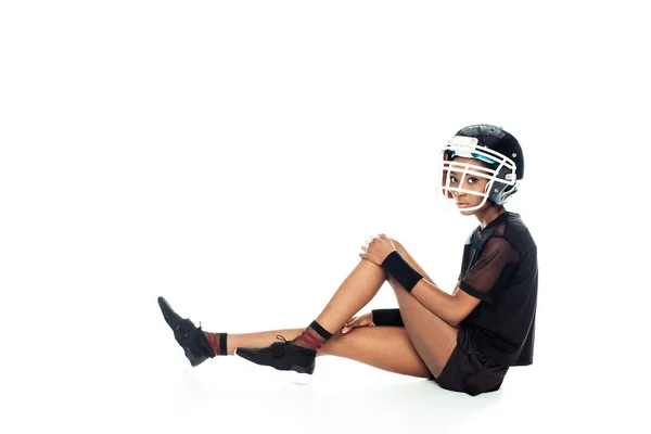 Vista lateral del jugador de fútbol americano femenino en el equipo que descansa en el piso aislado en blanco - foto de stock