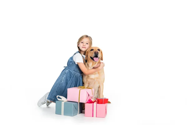Adorable enfant étreignant chien et assis à des boîtes-cadeaux, isolé sur blanc — Photo de stock