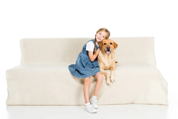 Criança sorridente e cão sentado no sofá, isolado no branco — Fotografia de Stock