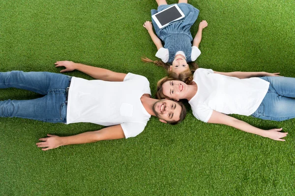 Overhead view of family with digital tablet lying on green grass — Stock Photo