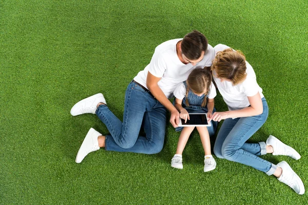 Вид семьи с помощью цифрового планшета, сидя на зеленой траве — стоковое фото