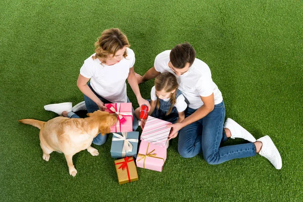 Vista de ángulo alto de la familia con regalos envueltos sentados sobre hierba verde - foto de stock