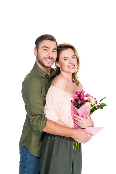 Smiling man hugging wife with bouquet of flowers and postcard isolated on white — Stock Photo