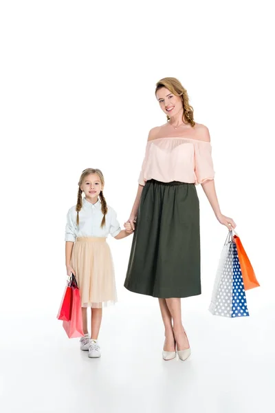 Stylish mother and daughter with shopping bags holding hands isolated on white — Stock Photo