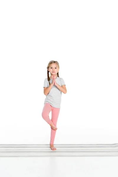 Criança praticando ioga no tapete de ioga isolado no branco — Fotografia de Stock