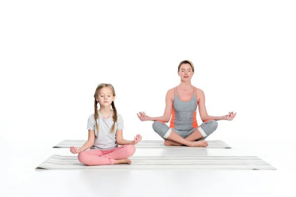 Mère athlétique et sa fille pratiquant le yoga sur des nattes ensemble isolé sur blanc — Photo de stock