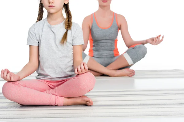 Vista parcial de la madre y la hija atléticas practicando yoga sobre esteras juntas aisladas en blanco — Stock Photo