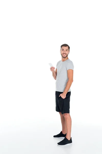 Hombre sonriente en ropa deportiva y auriculares escuchando música aislada en blanco - foto de stock