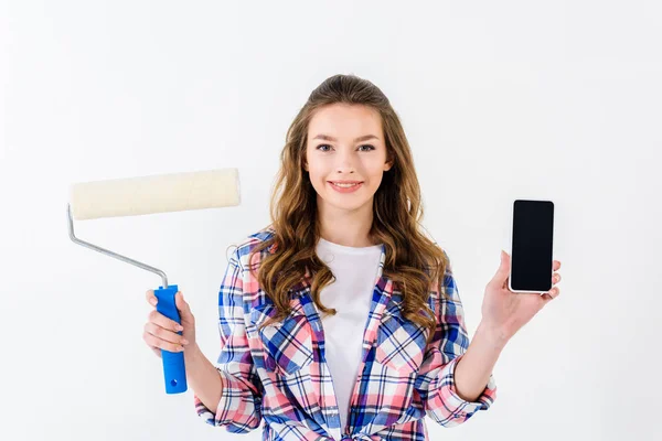 Menina sorrindo segurando pincel rolo de pintura e smartphone — Fotografia de Stock