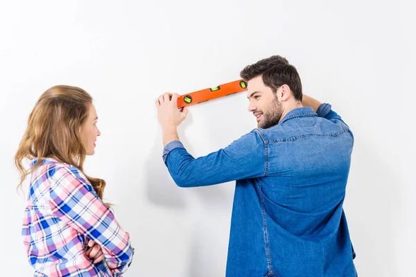 Rear view of boyfriend measuring wall flatness — Stock Photo