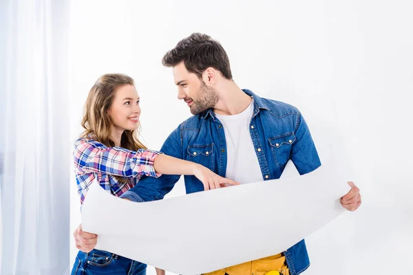 Smiling girlfriend pointing on blueprint to boyfriend — Stock Photo