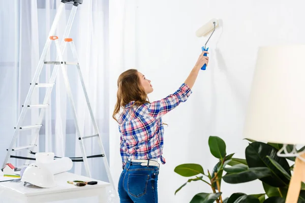 Vista laterale della ragazza pittura parete con vernice bianca — Foto stock