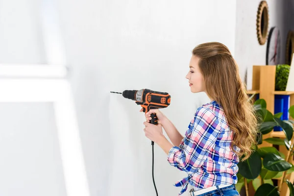 Side view of girl drilling wall — Stock Photo