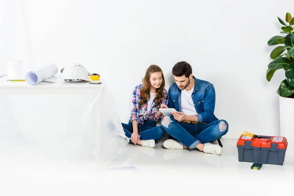 Усміхнена пара сидить на підлозі і використовує планшет — стокове фото
