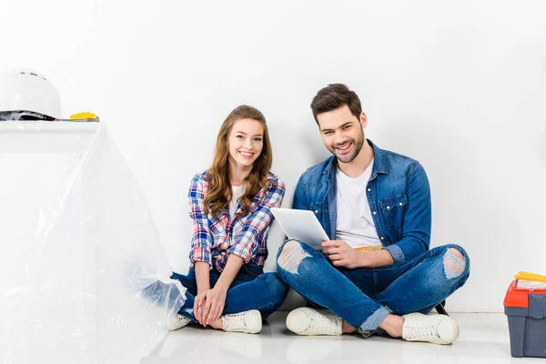 Couple souriant assis avec tablette et regardant la caméra — Photo de stock