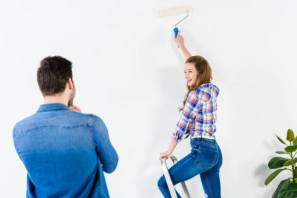 Sorrindo namorada pintura parede e olhando para o namorado — Fotografia de Stock