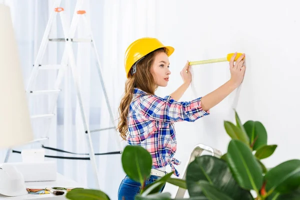 Young woman measuring wall with tape measure — Stock Photo