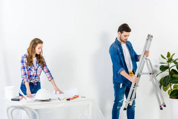 Boyfriend holding ladder and girlfriend looking at blueprint — Stock Photo