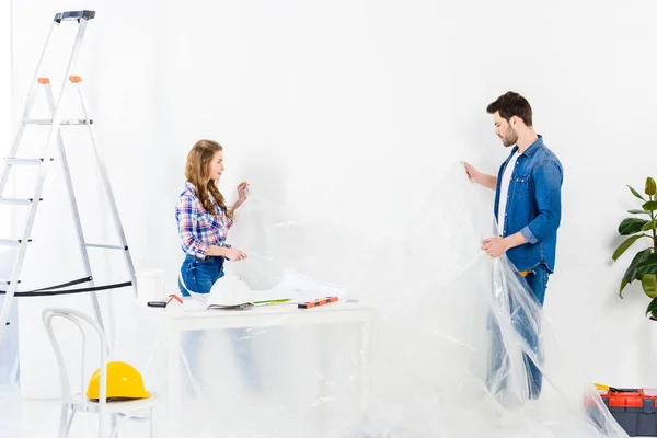 Casal segurando celofane ao fazer reparos em casa — Fotografia de Stock