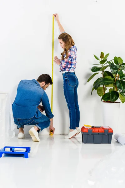 Pareja que mide la pared en casa nueva - foto de stock