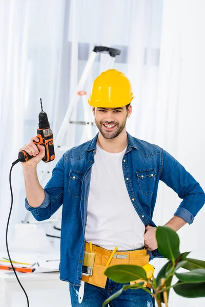 Lächelnder schöner Mann, der mit Bohrmaschine steht und in die Kamera schaut — Stockfoto