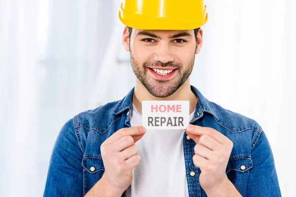 Sorrindo bonito homem segurando cartão de reparação em casa — Fotografia de Stock