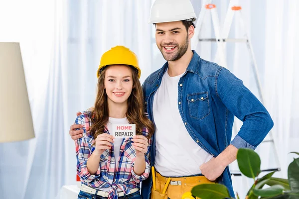 Smiling couple in helmets holding home repair card — Stock Photo