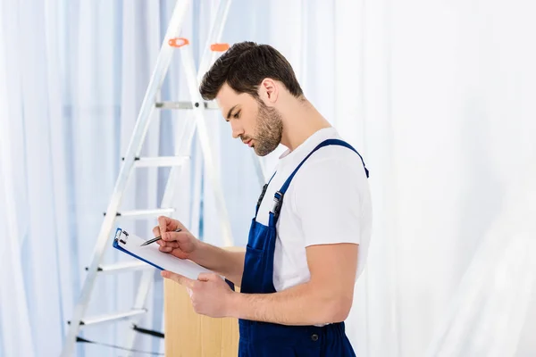 Seitenansicht eines durchdachten Umzugsmitarbeiters, der in die Zwischenablage blickt — Stockfoto