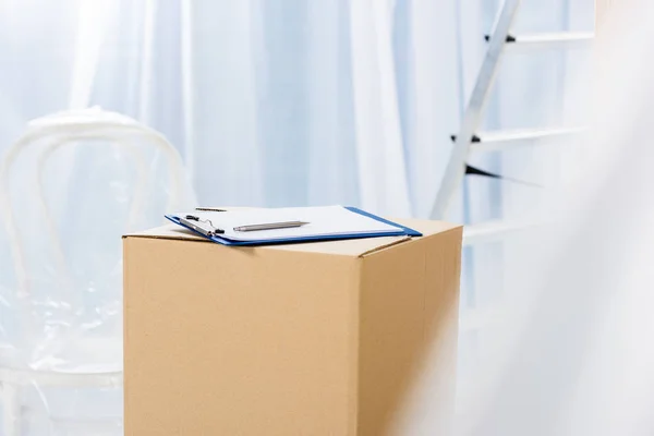 Clipboard with pen on box in empty room — Stock Photo