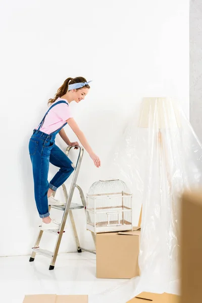 Menina de pé na escada e tomando gaiola pássaro — Fotografia de Stock